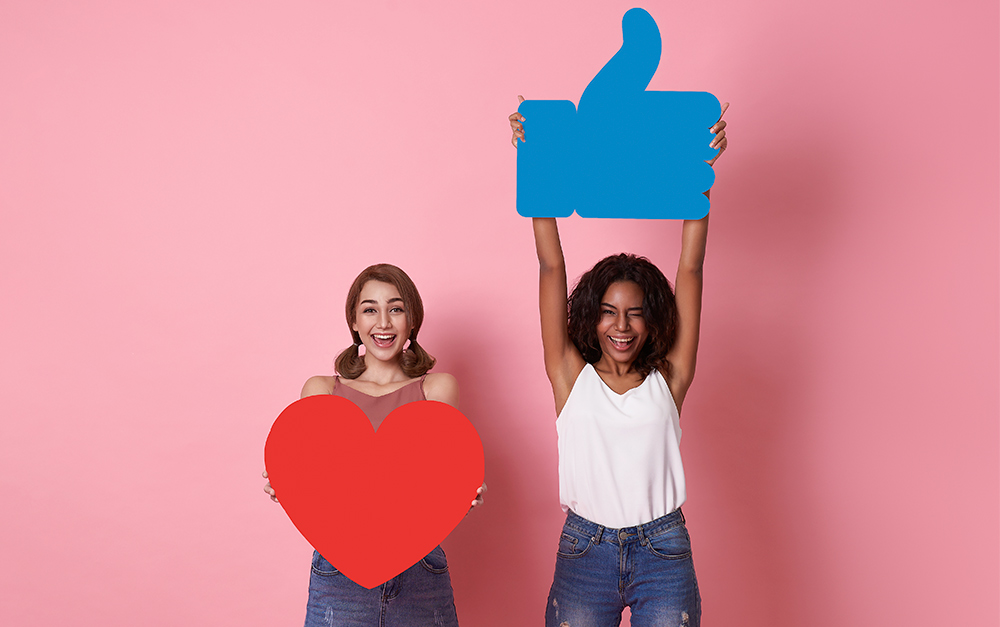 Imagem que mostra duas mulheres segurando símbolos de curtida e comentário que são realizados nos posts de Facebook.